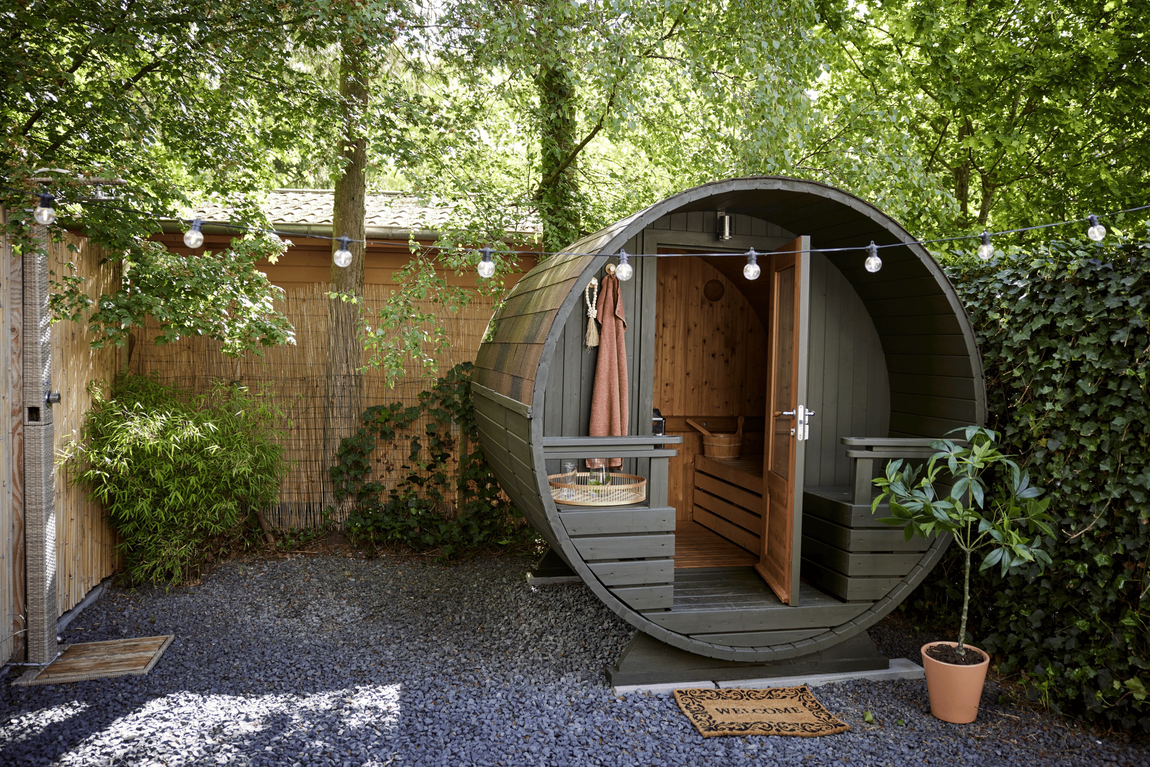 Une structure en bois en forme de tonneau, dotée d’une porte, d’un petit espace pour s’asseoir et d’un paillasson.