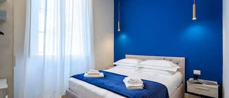 A bedroom with a bed, a nightstand, a window with curtains, and a blue wall.