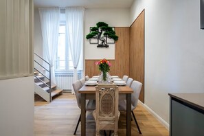 A dining area with a wooden table set for six, a decorative tree wall art, and a staircase leading to an upper level. - Relax Retreat in Historic Florence - Private Sauna & Hydromassage (Firenze)