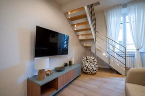 A modern living room with a flat-screen TV, a console table, a patterned armchair, and a staircase with a railing. - Relax Retreat in Historic Florence - Private Sauna & Hydromassage (Firenze)