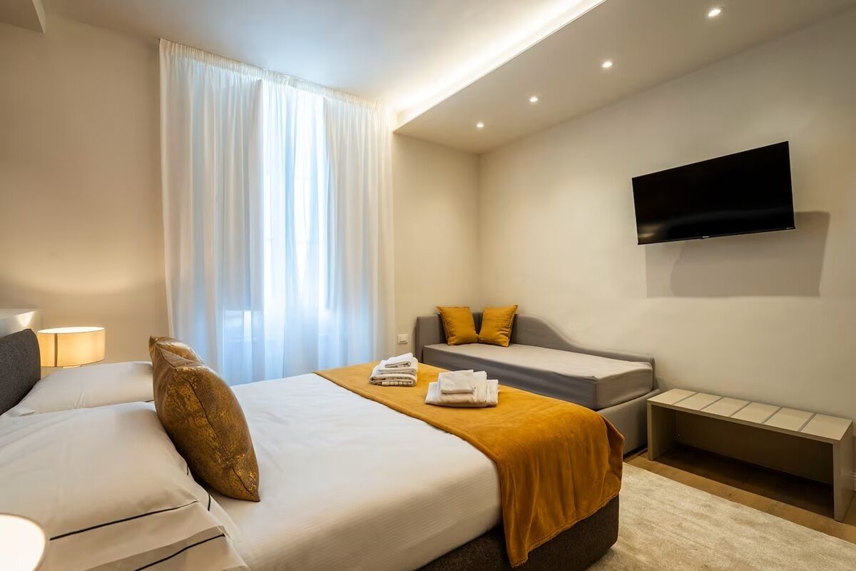A hotel room with a bed, a sofa, a flat-screen TV, and a bedside table.