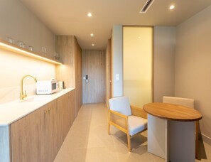 A modern kitchen with a white countertop, gold faucet, and a microwave. There is a wooden door and a chair with a cushion. - Apartment La Plaza 2 Deluxe With Balcony (Alicante)