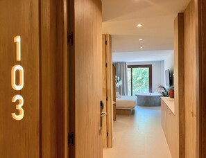 A hotel hallway with wooden doors marked with numbers, a bed, a bathtub, and a window with a view of greenery. - Apartment La Plaza 2 Deluxe With Balcony (Alicante)