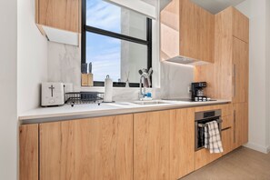 A modern kitchen with wooden cabinets, a built-in oven, a coffee machine, and a window above the sink. - The Crosby Worldcenter 2BR Palermo Home  (Miami)