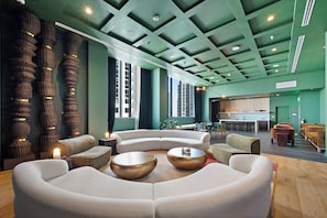 A modern lounge area with a curved white sofa, a round gold table, and a bar area in the background. - The Crosby Worldcenter 2BR Palermo Home  (Miami)