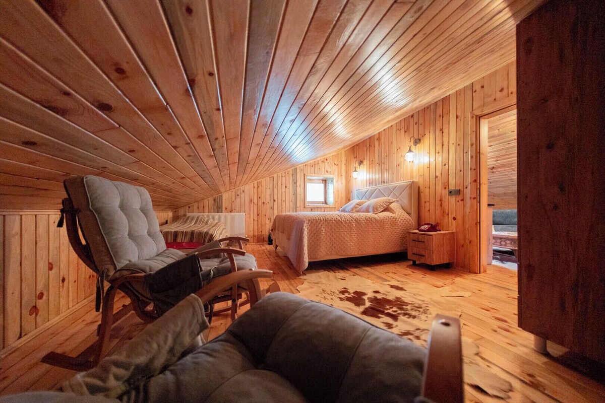 A cozy wooden cabin interior with a bed, a chair, and a small table.