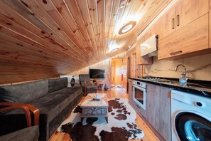 Un espacio habitable compacto con sofá, mesa de centro, televisión y zona de cocina con lavadora.