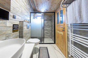A modern bathroom with a wooden ceiling, a white bathtub, a toilet, and a glass-enclosed shower area. - Mudurnu Aşiyan Evleri (Mudurnu)