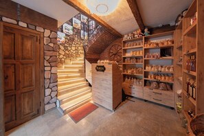 A rustic interior with a stone staircase, wooden shelves stocked with goods, and a wooden door.