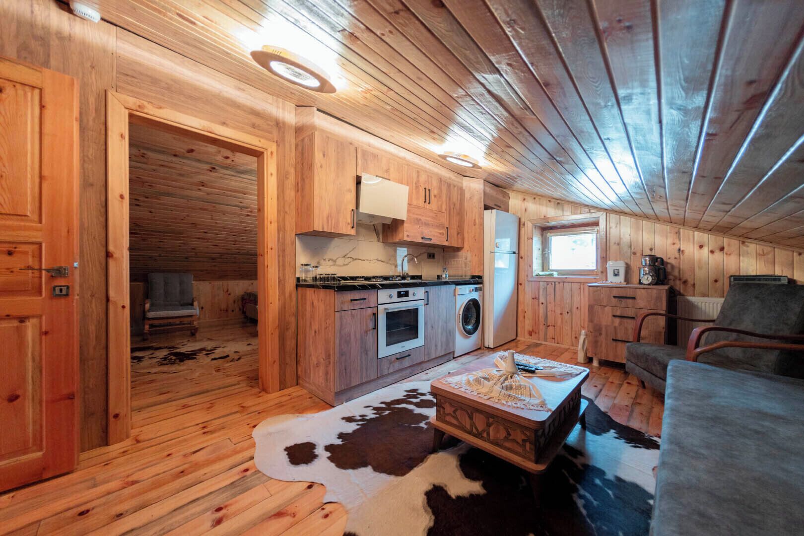 A cabin interior with a wooden floor, a kitchen with modern appliances, a cowhide rug, and a cozy seating area.