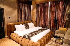 Quarto com cama grande, uma cadeira e cortinas.