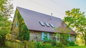 Uma casa de madeira rústica com telhado inclinado, escada de madeira e um quintal cercado.