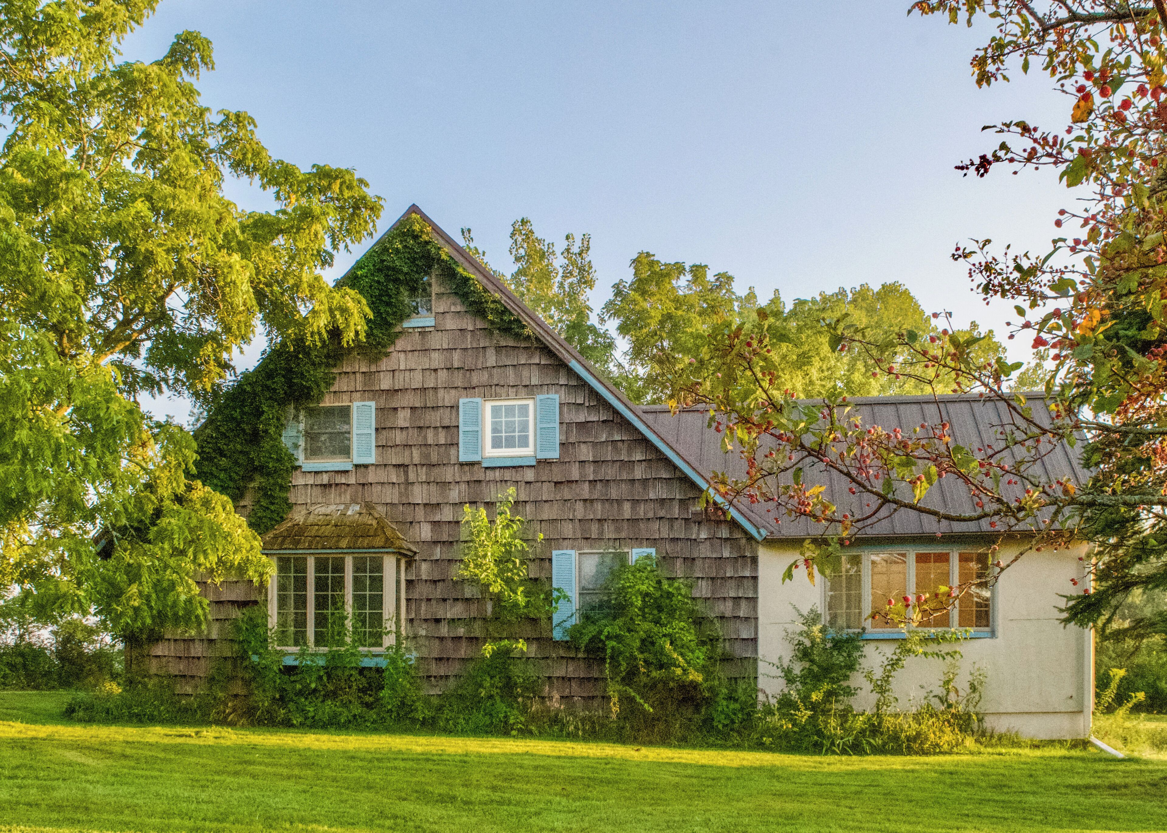 A two-story house with a sloped roof, surrounded by a grassy yard and trees.