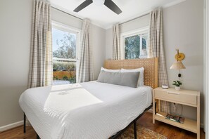Ein Schlafzimmer mit einem Bett, einem Nachttisch mit Lampe und Blick ins Freie.