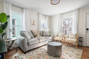 A living room with a grey sofa, striped pillows, a patterned rug, a round coffee table, and a view of a balcony. - Moultrie & Palmetto Suites | Walk to Bars (Charleston)