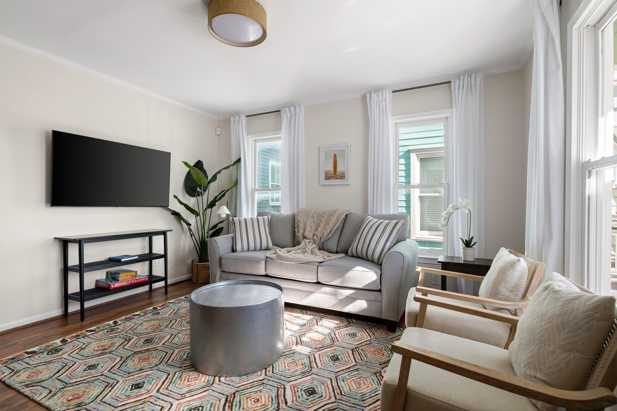 Ein Wohnzimmer mit Sofa, Sesseln, Couchtisch, Fernseher und einem gemusterten Teppich.