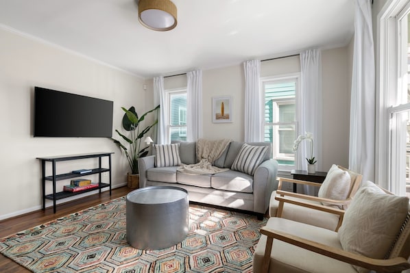 A living room with a sofa, armchair, coffee table, TV, and a patterned rug. - Moultrie & Palmetto Suites | Walk to Bars (Charleston)