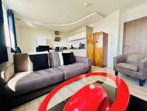 A modern living room with a grey sofa, a red accent piece, and a wooden wardrobe. - Modern Flat | Old Town Views, Central Ipswich (Suffolk)