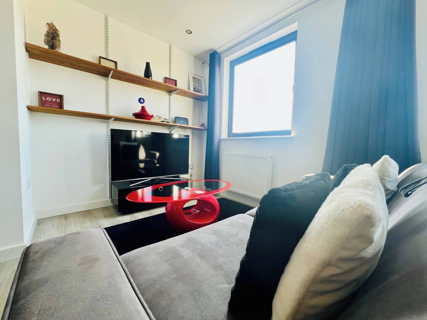 A modern living room with a flat-screen TV, a red glass coffee table, and a grey sofa.