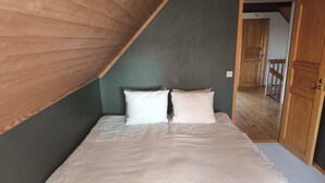 A bedroom with a sloped ceiling, a bed with patterned bedding, and a wooden door.