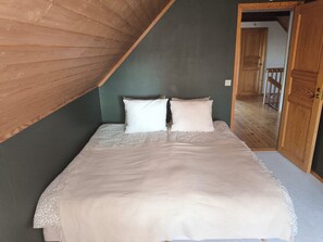 Un dormitori amb sostre inclinat, un llit amb roba de llit estampada i una porta de fusta.