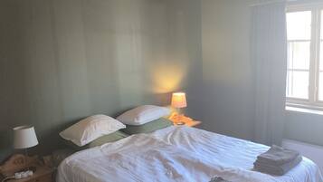 A bedroom with a wooden ceiling, a bed with white bedding, a nightstand with a lamp, and a window with curtains.