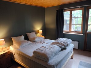 A bedroom with a large bed, two bedside lamps, a window with curtains, and a radiator. - Scandinavian Forest Retreat • Sauna • Fireplace • Nature Experiences (Åsensbruk)