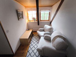 Een kleine kamer met een witte bank, een houten krukje en een radiator.
