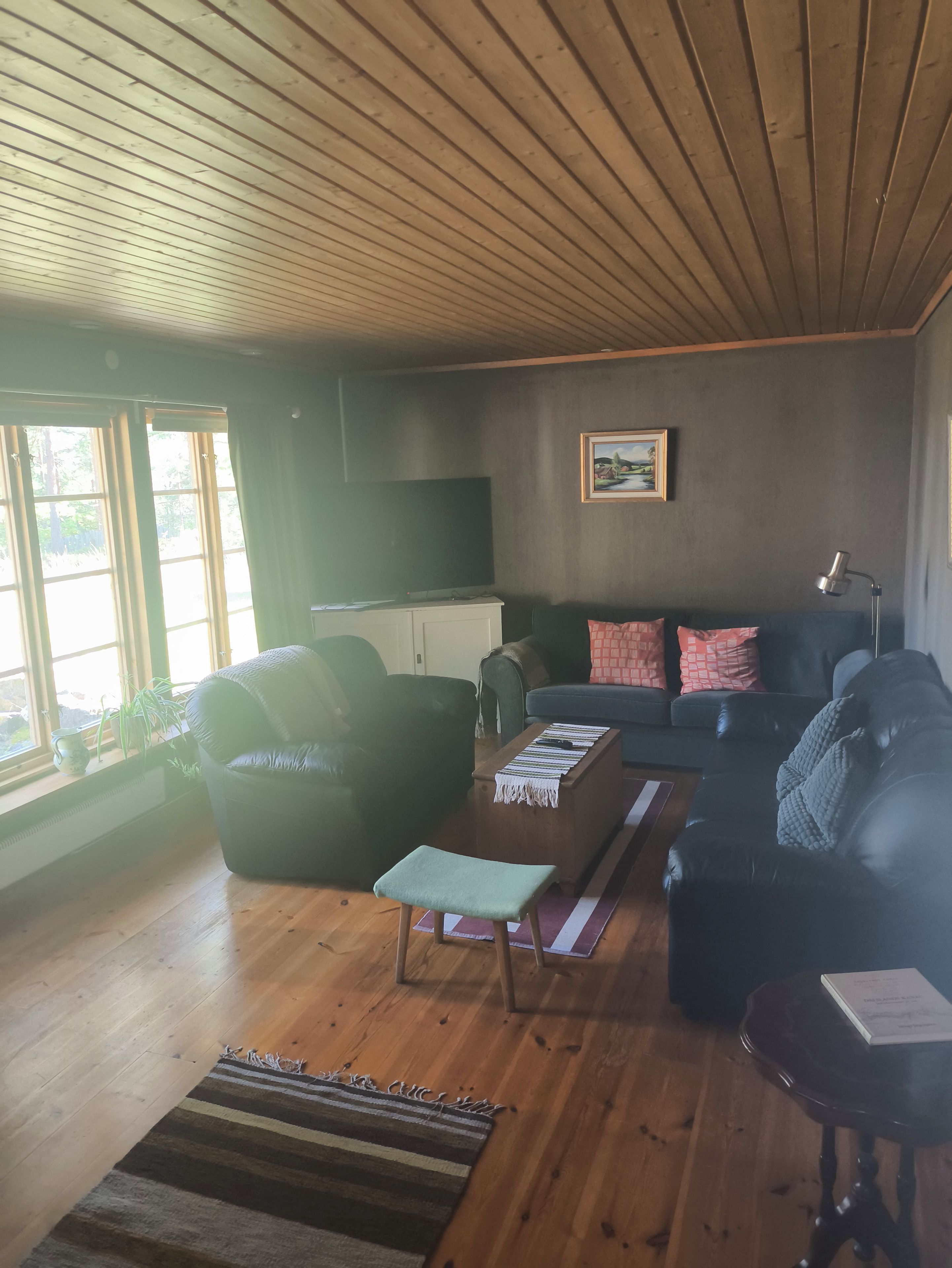 A living room with a wooden ceiling, a sofa, a coffee table, a small stool, and a lamp.