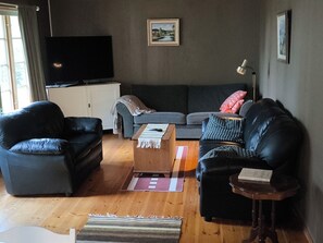 Una sala de estar con sofá, dos sillones, una mesita de centro, televisor y lámpara.