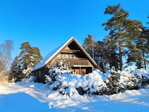 Una cabana de fusta amb teulada triangular envoltada d'arbres coberts de neu.