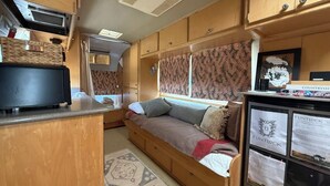 A compact RV interior with a kitchenette, a sofa bed, and a small entertainment unit.