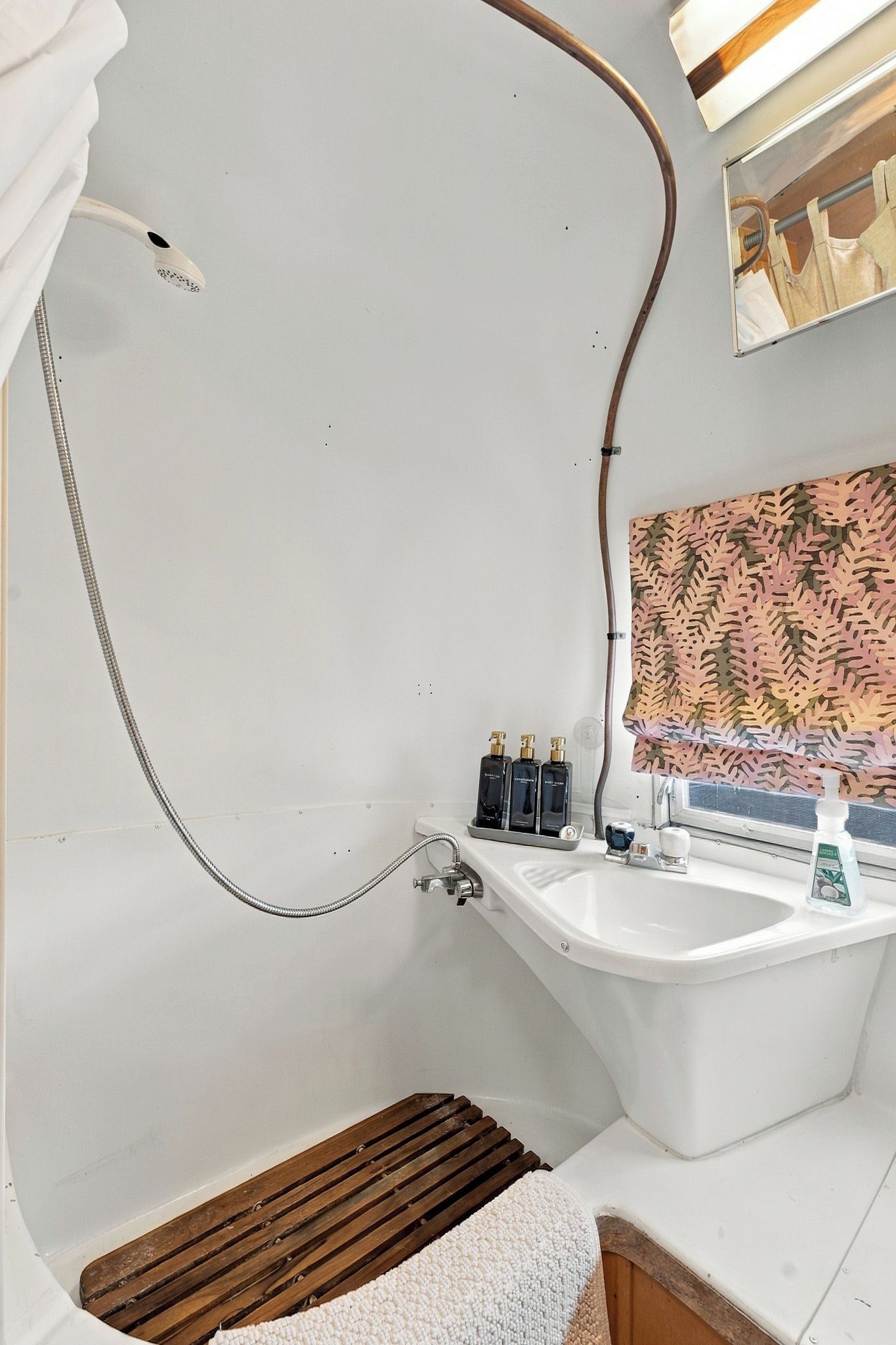 A bathroom with a white bathtub, a shower, and a sink. There are two bottles of liquid soap on the sink.