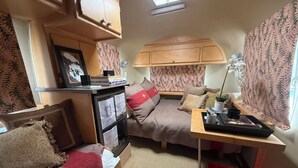 Ein kompaktes Wohnmobil-Interieur mit einer Küchenzeile, zwei Schlafbereichen und einem kleinen Tisch mit einer Lampe.