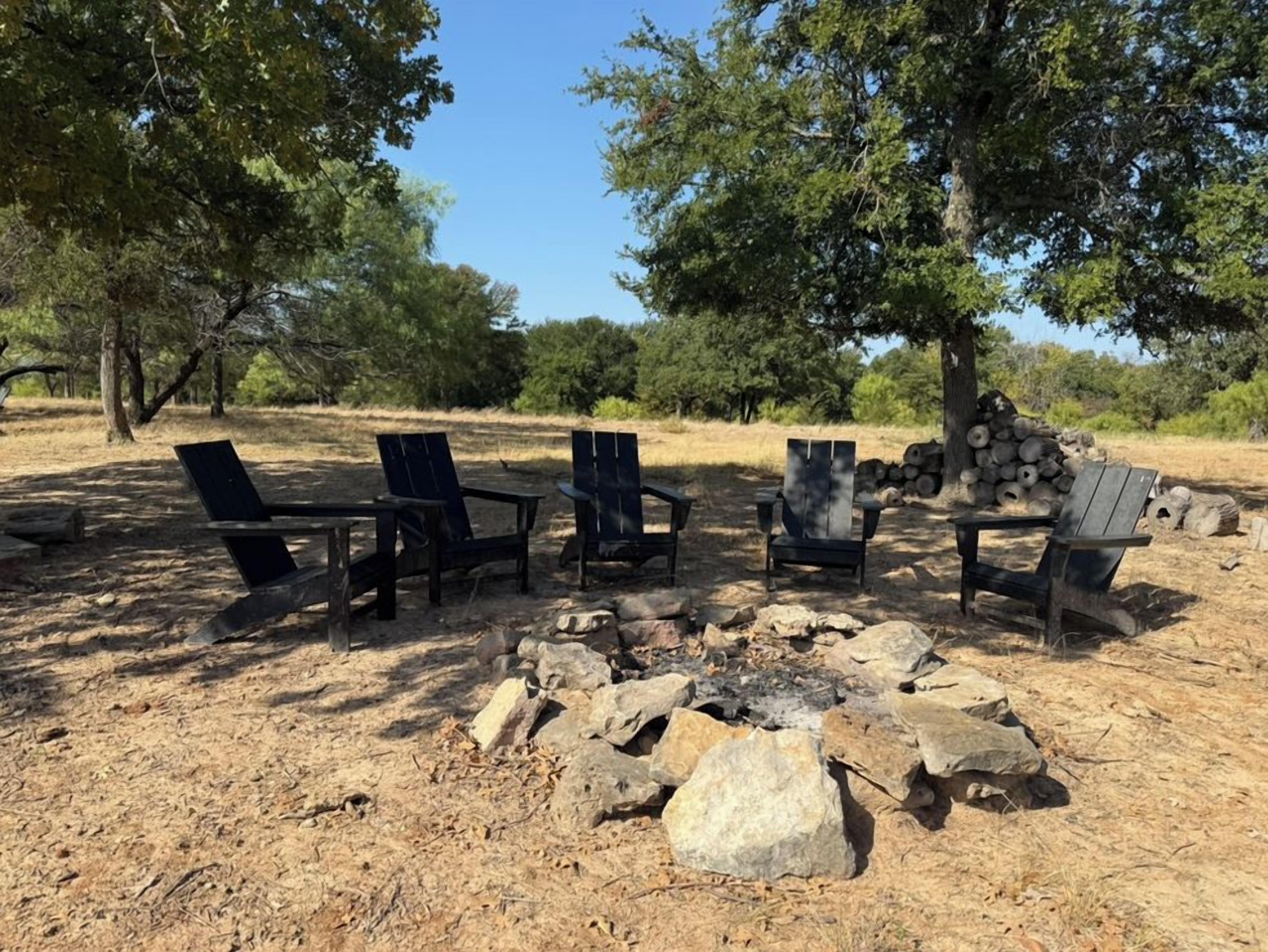An outdoor seating area with a fire pit surrounded by rocks, under trees.