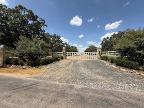 A gated driveway leading to a building with a stone wall on one side and a metal gate.