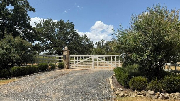 A gated driveway leading to a property with a gravel path and a stone wall on one side.