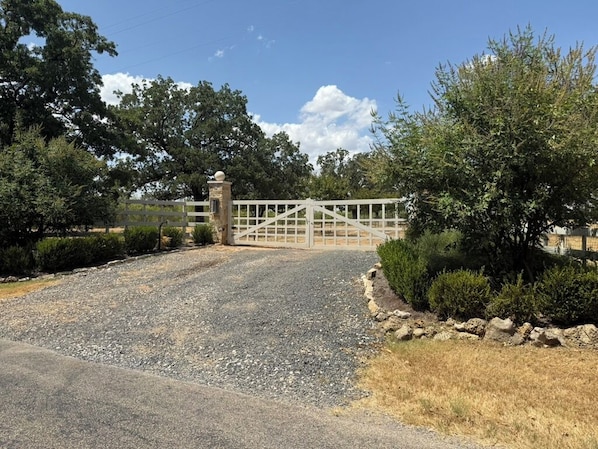 A gated driveway leading to a property with a gravel path and a stone wall on one side.