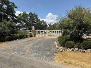 A gated driveway leading to a property with a gravel path and a stone wall on one side.