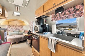 A compact RV kitchen with a microwave, coffee maker, and a sink.