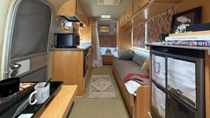 A compact RV interior with a kitchenette, a sleeping area, and a small dining space.