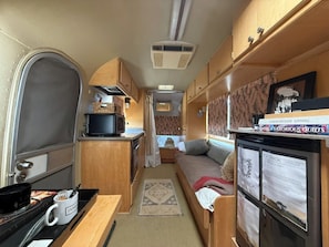 A compact RV interior with a kitchenette, a sleeping area, and a small dining space.