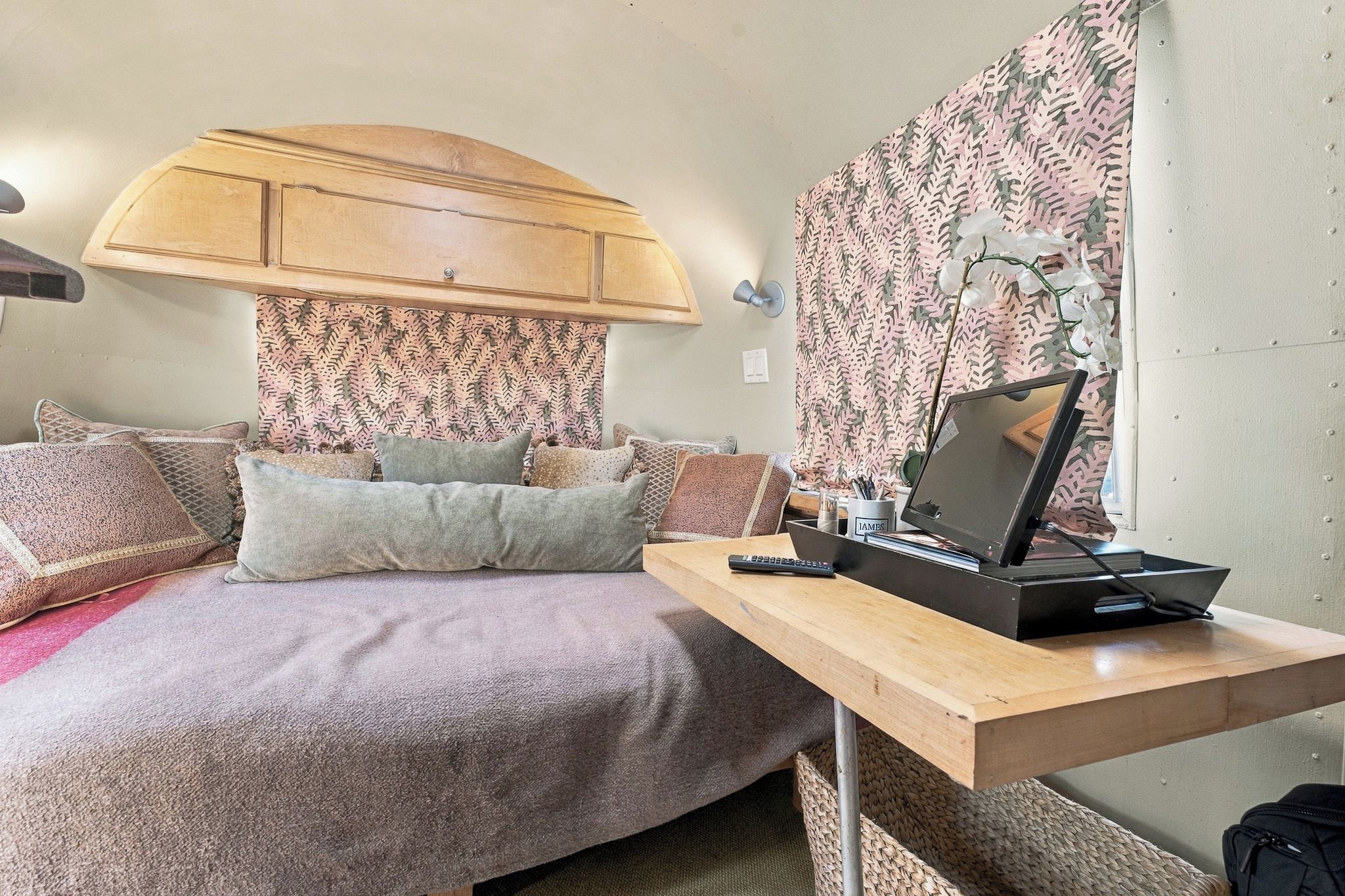A bedroom with a bed, pillows, a desk with a computer, and a wall-mounted lamp.
