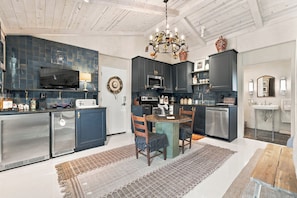 A modern kitchen with dark cabinetry, a dining area with a wooden table and chairs, and a chandelier.