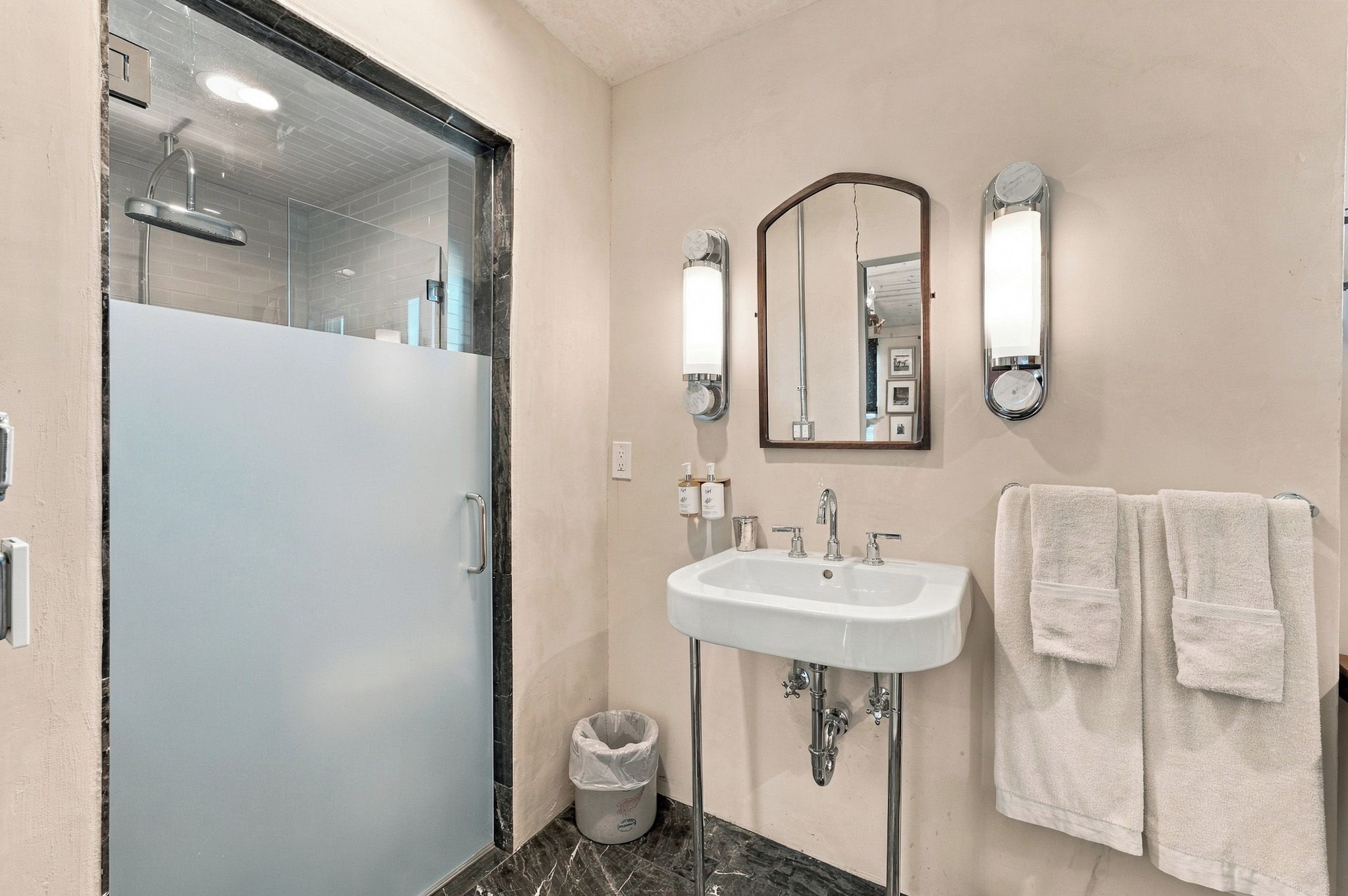 Une salle de bain avec une douche à parois de verre, un lavabo blanc avec un miroir au-dessus, et deux serviettes suspendues sur un porte-serviettes.