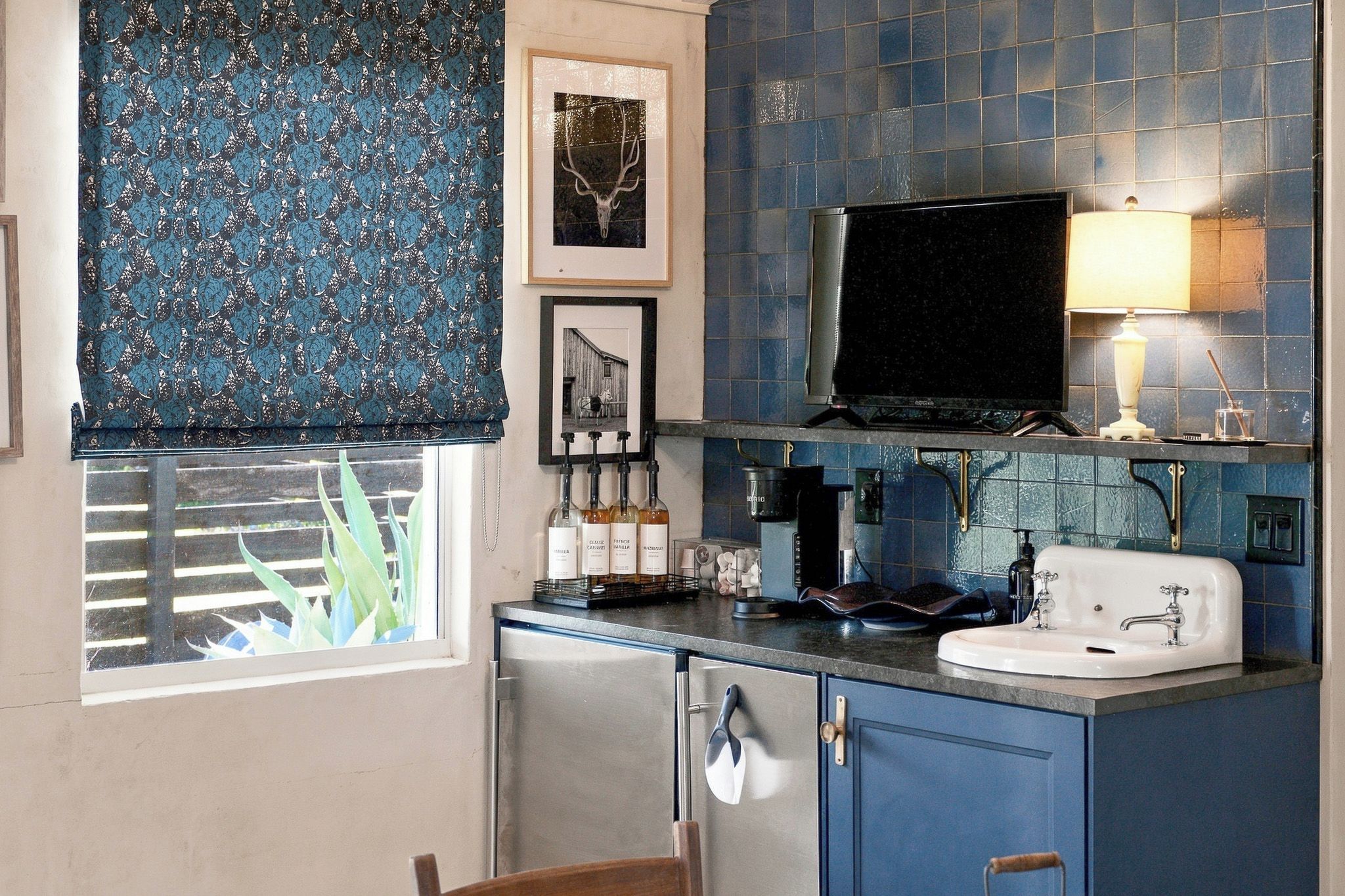 A compact kitchen with a window, a sink, a stove, and a television.