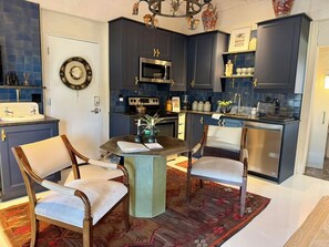 A modern kitchen with dark cabinetry, a central island, and a dining area with chairs.