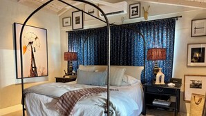 Ein Schlafzimmer mit Himmelbett, Baldachin, Nachttisch, Lampe und einer an der Wand montierten Ablagefläche.