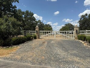 A gated driveway leading to a property with a gravel surface and a wooden fence.