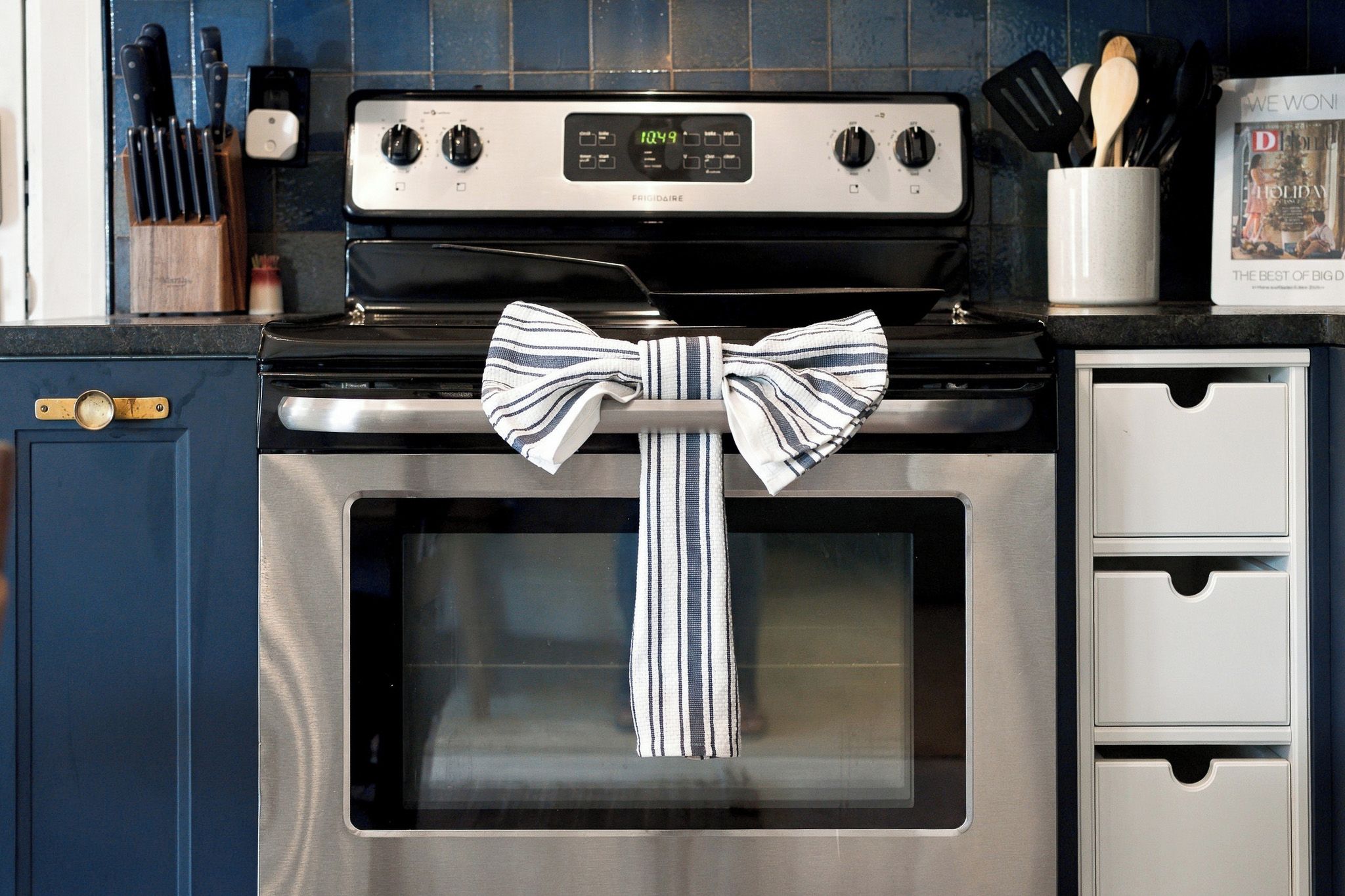 A kitchen with a stainless steel stove, a digital clock, and a striped towel tied around the oven door handle.